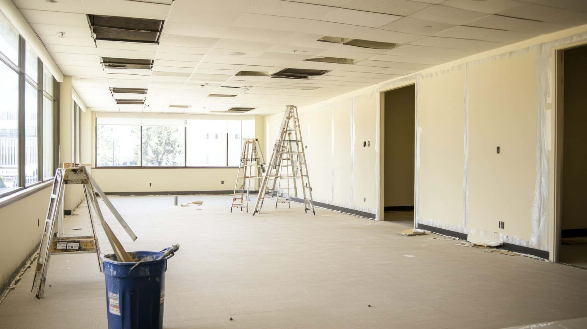 An empty corporate office during renovation, with the walls prepped for painting and renovation tools like ladders and scaffolding set up